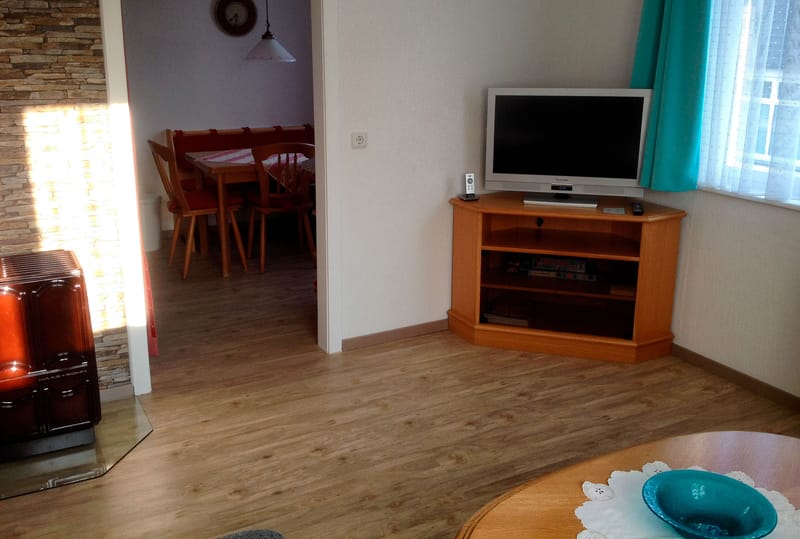 Wohnzimmer mit Fernseher in der Ecke, im Hintergrund der Essbereich