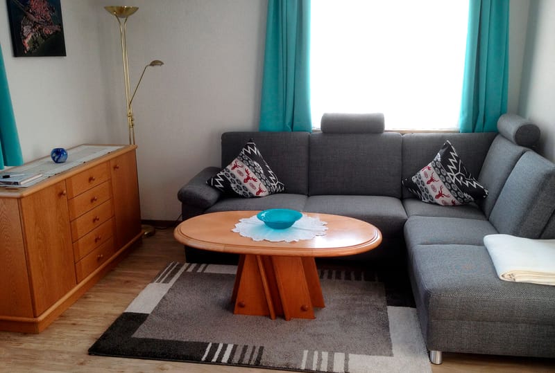 Wohnzimmer mit grauem Ecksofa, rundem Holztisch und türkisfarbenen Vorhängen