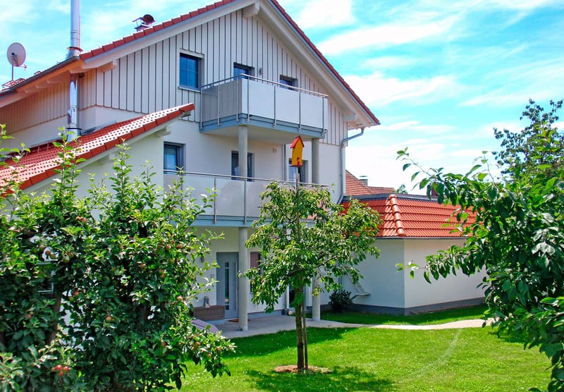 Das Haus mit Balkonen von der Gartenseite, davor Rasen und ein Apfelbaum