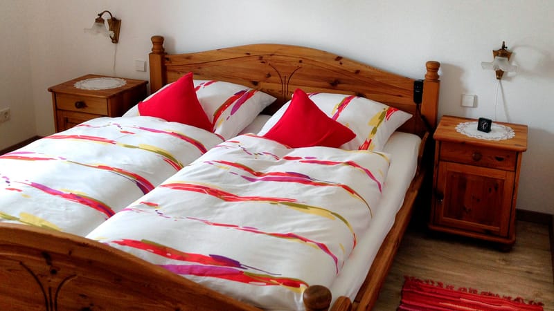 Schlafzimmer mit Holz-Doppelbett, bunt gestreifter Bettwäsche und roten Kissen