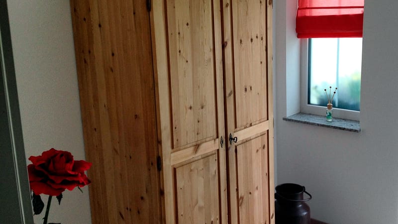 Kleiderschrank aus hellem Holz neben einem Fenster im Schlafzimmer