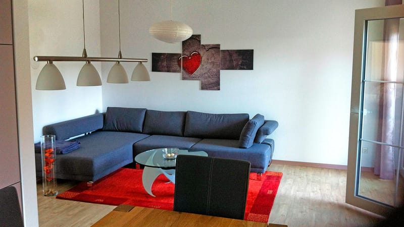 Wohnbereich mit blauem Sofa, rotem Teppich und Hängelampen