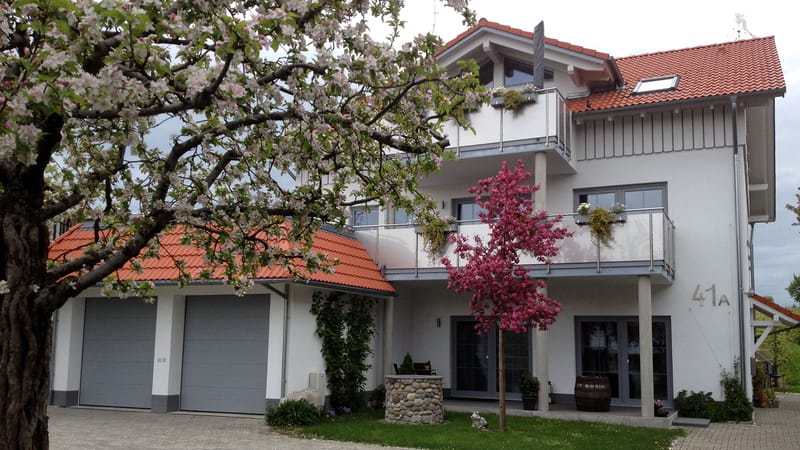 Das Haus mit Balkonen und zwei Garagen, davor ein blühender Baum und die Hausnummer 41a