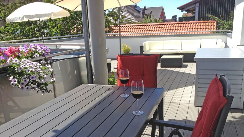 Sitzplatz im Freien mit Tisch, zwei Weingläsern, roten Stühlen und Blumenkasten