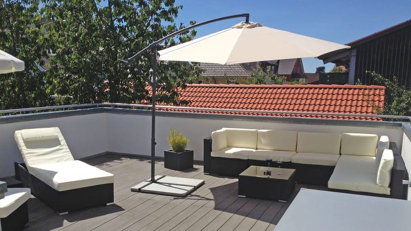Sitzbereich im Freien mit Loungemöbeln, Sonnenliege und aufgespanntem Sonnenschirm