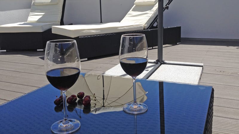 Zwei Gläser Rotwein auf einem Tisch, dahinter Sonnenliegen